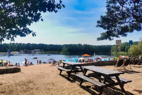 Słoneczny dzień nad jeziorem Średnim Turawa. Ludzie odpoczywają na plaży, kąpią się i pływają.
