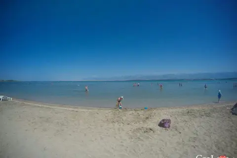Piaszczysta plaża w Chorwacji z ludźmi kąpiącymi się w morzu i dzieckiem bawiącym się na piasku.