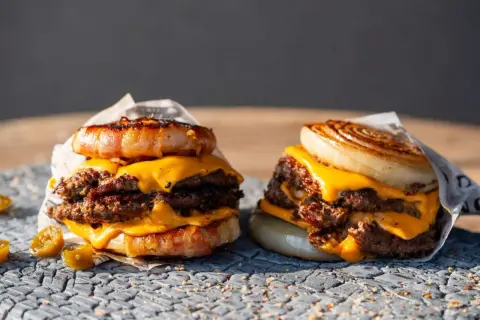 Zwei saftige "Flying Dutchman Burger" mit doppelt Fleisch, geschmolzenem Käse und einer Zwiebel- bzw. Speckkrone.