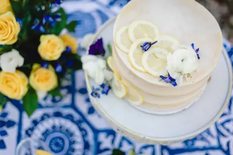 Gâteau de mariage jaune et bleu, décoré de rondelles de citron et de fleurs. Un bouquet de roses jaunes et de fleurs bleues est à proximité.