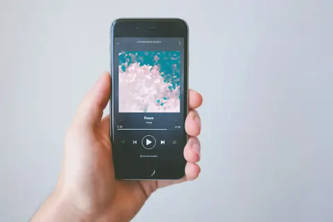 A hand holds a smartphone displaying the Spotify app, showing the song "Peace" by ramp. This image illustrates how to get music on Spotify.