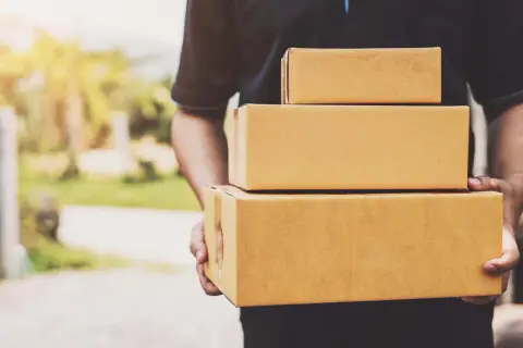 Kurier firmy kurierskiej FedEx niesie trzy paczki.