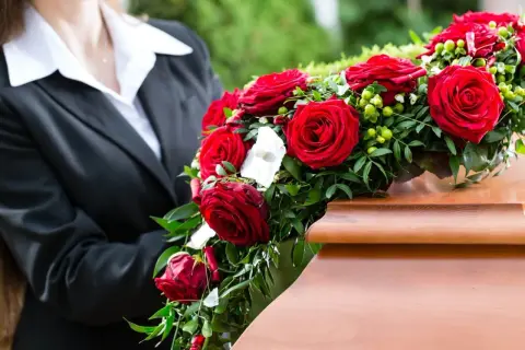 Osoba w czerni kładzie wieniec pogrzebowy z czerwonych róż na trumnie. Wieniec pogrzebowy znaczenie to symbol miłości i pamięci.