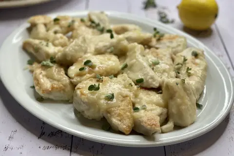 Delizioso pollo al limone ricetta, servito su un piatto bianco con erbe aromatiche e un limone sullo sfondo.