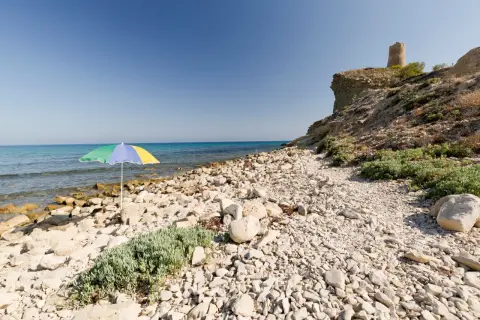 Sombrilla de colores en la playa de las covaticas, con mar turquesa y torre antigua en el acantilado.