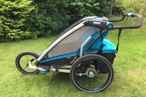 En Thule Chariot Sport 2 barnvagn står på en gräsmatta. Den är blå och svart med stora hjul.