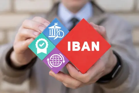 Ręce trzymają puzzle z napisem IBAN i ikonami: bank, pieczęć jakości, globalny zasięg.
