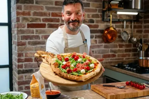 Ein Mann präsentiert stolz eine köstliche Pizza mit Rucola, Kirschtomaten und Mozzarella. Perfekt für einen gemütlichen Pizza Abend!
