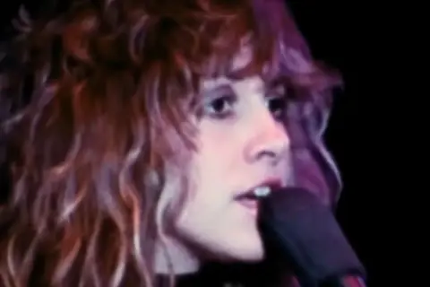 Stevie Nicks śpiewa "Dreams" Fleetwood Mac, jej charakterystyczne falujące włosy i intensywne spojrzenie.