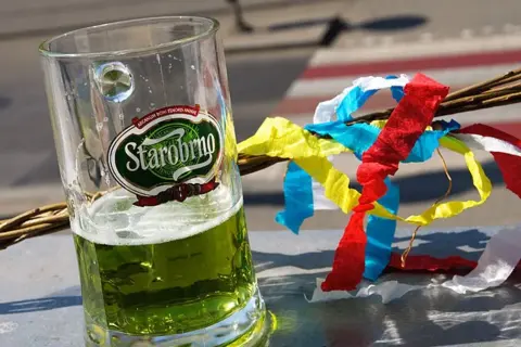 Szklanka zielonego piwa czeskiego Starobrno obok wierzbowej rózgi z kolorowymi wstążkami.
