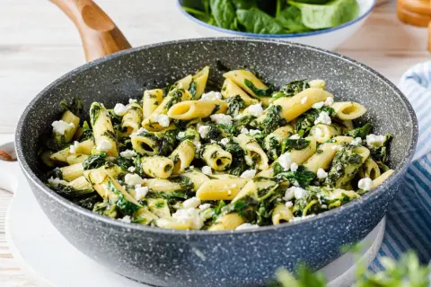 Penne-Nudeln mit Spinat und zerbröseltem Feta in einer Pfanne.