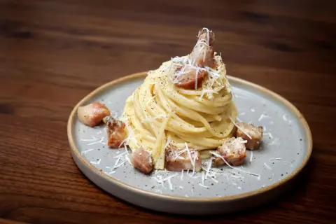 Pyszne spaghetti carbonara z chrupiącym guanciale, posypane parmezanem i świeżo mielonym pieprzem.