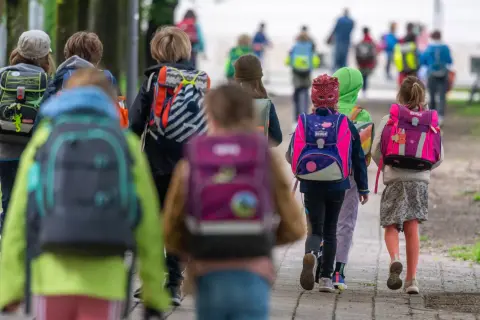 Kinder mit bunten Schulranzen gehen gemeinsam auf dem Weg zur Grundschule. Ein sicherer Schulweg ist wichtig für alle.