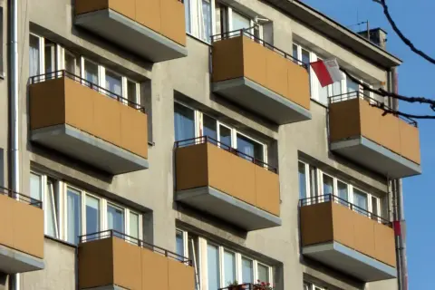 Szukasz informacji, jak dostać mieszkanie komunalne w Łodzi? Zobacz fasadę bloku z żółtymi balkonami i polską flagą.