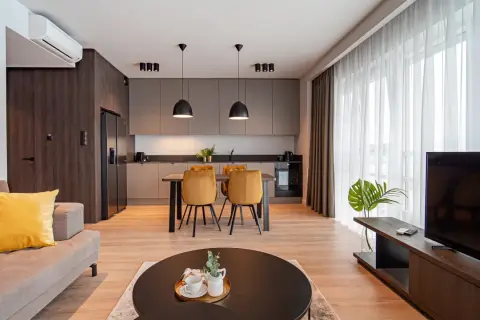Nowoczesny salon z aneksem kuchennym w hotelu Platinum Residence. Kanapa, stół z krzesłami, kuchnia i TV.
