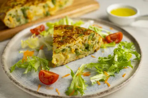 Pyszny omlet z piekarnika z fasolką szparagową i marchewką, podany z sałatką i pomidorkami.