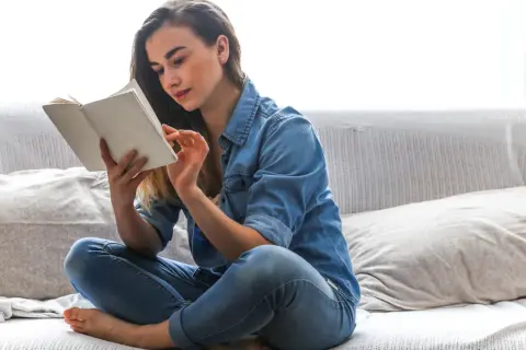 Odkryj sekrety domowych bibliotek gwiazd! Co naprawdę czytają znani i lubiani? Młoda kobieta w dżinsowej koszuli zanurzona w lekturze na kanapie.