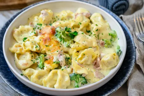 Cremiger Tortellini Auflauf mit Brokkoli und Schinken, überbacken mit Käse und bestreut mit Petersilie. Ein köstliches Gericht!