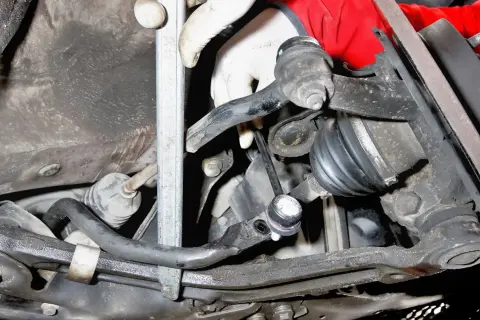 Montaż łącznika stabilizatora Toyota Yaris 1. Widoczna ręka w rękawiczce przykręca element zawieszenia.