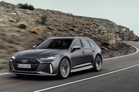 Szary Audi RS6 Avant pędzi po krętej drodze wśród skalistych wzgórz.