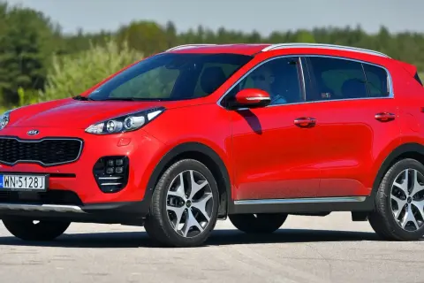 Czerwony Kia Sportage 1. generacji z kierowcą w okularach przeciwsłonecznych jedzie po drodze.