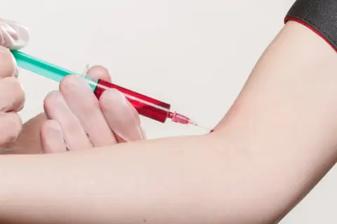 Prélèvement sanguin : une seringue verte et rouge est insérée dans un bras.