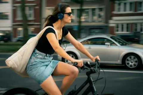 Frau fährt Fahrrad mit Kopfhörern und Tasche. Ob man mit AirPods Fahrrad fahren darf, ist eine Frage der Sicherheit und des Gehörs.