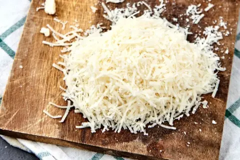Stos parmezanu startego na drewnianej desce, gotowy do posypania ulubionego dania.
