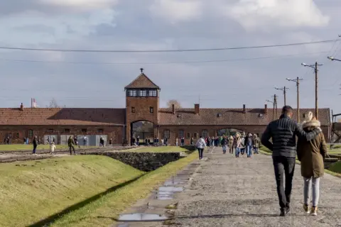 Spacer po terenie Państwowego Muzeum Auschwitz-Birkenau w Oświęcimiu. Ludzie zwiedzają teren dawnego obozu.