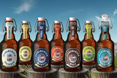 Flensburger Pils Bier Marken am Strand. Eine Möwe fliegt über das Meer, während die Flaschen mit Bügelverschluss im Gras stehen.