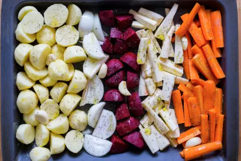 Ugnsrostade rotfrukter: potatis, morötter, palsternacka, rödbetor och lök, kryddade och redo för ugnen.