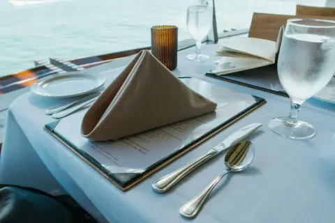 Stół w restauracji z widokiem na morze, nakryty do posiłku, z menu i kieliszkiem wody.
