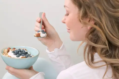 En kvinna äter en skål med yoghurt, blåbär och nötter. En hälsosam frukost som passar bra för diabetes typ 2 kost.