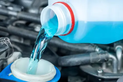 Blaues Scheibenwischwasser wird aus einem Behälter in den Einfüllstutzen gegossen.