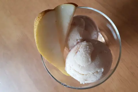 Ein Glas mit cremigem birnen eis, garniert mit einer frischen Birnenspalte, steht auf einem Holztisch.