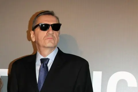 Władysław Pasikowski w czarnym garniturze i okularach przeciwsłonecznych, gotowy na premierę swojego kolejnego filmu.