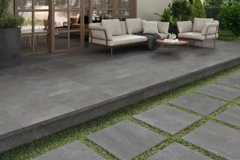 Terraza moderna con suelo de baldosas grises, ideal para pintar y renovar tu espacio exterior. Muebles de exterior y plantas verdes.