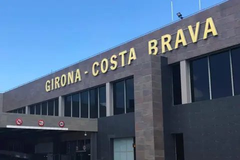 Złote litery "GIRONA - COSTA BRAVA" na nowoczesnym budynku lotniska.