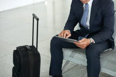 Biznesmen w garniturze z walizką czeka na lot. Jego praca poza miejscem zamieszkania wymaga częstych podróży.