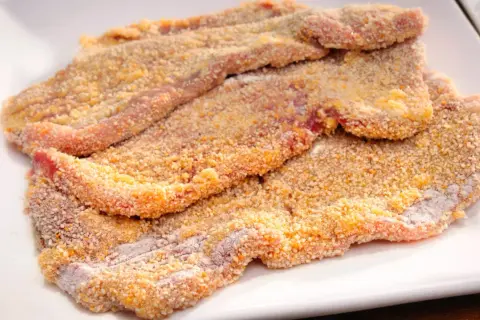 Mehrere panierte Schnitzel liegen auf einem weißen Teller, bereit für ein köstliches Schnitzel Rezept.