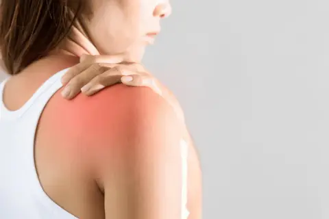 En person håller sin axel där en röd fläck indikerar muskelinflammation i armen.