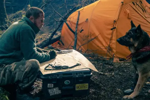 Man och hund vid orange tält, planerar en expedition. Kanske är det hjärtat av besten de söker.