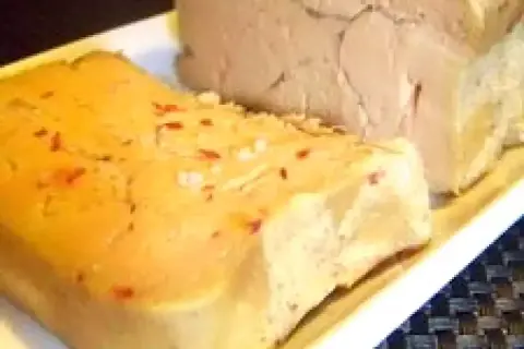 Deux blocs de foie gras sur une assiette blanche. L'un est parsemé de sel et de piment rouge, prêt pour une recette de foie gras au sel sans cuisson.