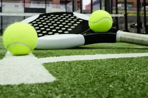 Raqueta de pádel y pelotas sobre césped artificial padel. La cancha está lista para el juego.