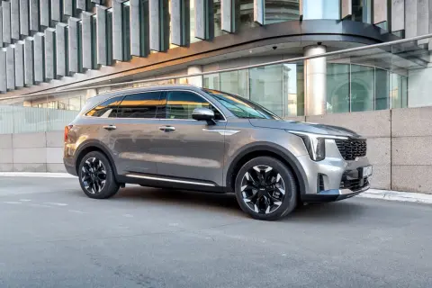 Elegancka, szara nowa Kia Sorento z czarnymi felgami stoi przed nowoczesnym budynkiem.