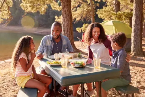 Familia disfrutando un picnic junto a un lago, una escena perfecta de qué hacer en familia al aire libre.