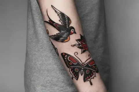 Tatuaż w stylu old school na przedramieniu: jaskółka, motyl i róża.