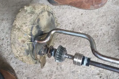 Zestaw naprawczy przekładni napędu kosiarki z zabrudzonym kołem i elementami mechanizmu.