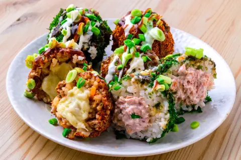 Sechs bunte Onigiri mit verschiedenen Füllungen und Toppings, umgeben von Frühlingszwiebeln und Saucen.
