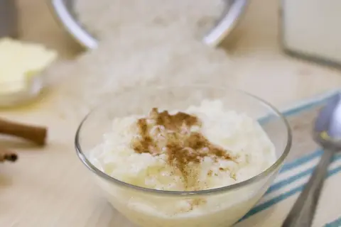 Schüssel mit Milchreis, Zimt, Butter, Zimtstangen und Reis. Die Frage, wie lange ist Milchreis nach MHD haltbar, beschäftigt viele.